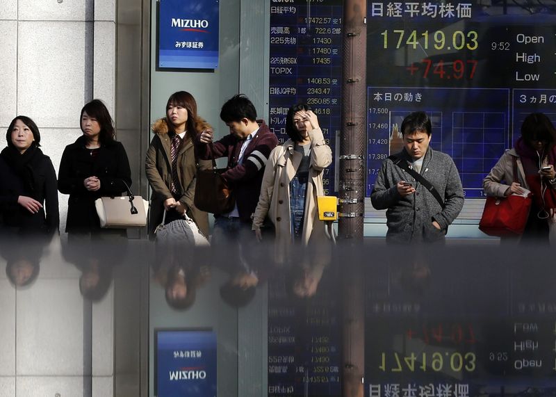 © Reuters. People standing in front of an electronic board showing the Japan's nikkei average outside a brokerage are reflected in a polished stone surface in Tokyo