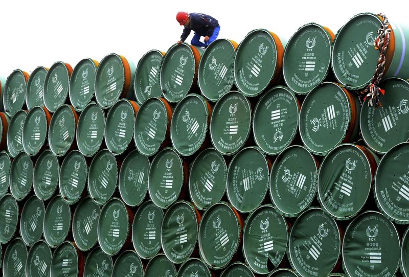 © Reuters. A worker stands on buckets of steel pipes which are waiting to be loaded onto a cargo ship, at a port in Lianyungang