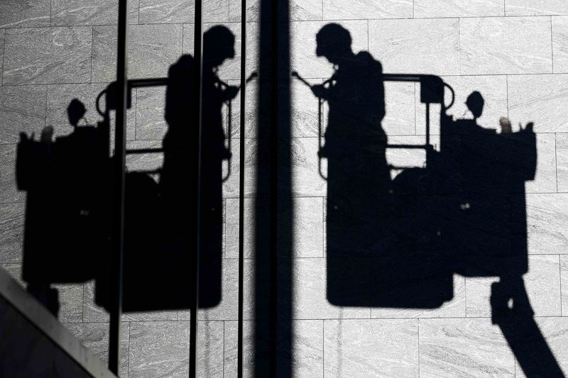 © Reuters. A worker's silhouette is reflected in a window as he stands on a cherry picker in Tokyo