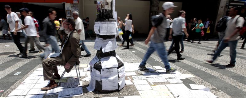 © Reuters. Promotor de vagas sentado perto de lista de empregos numa rua importante de São Paulo