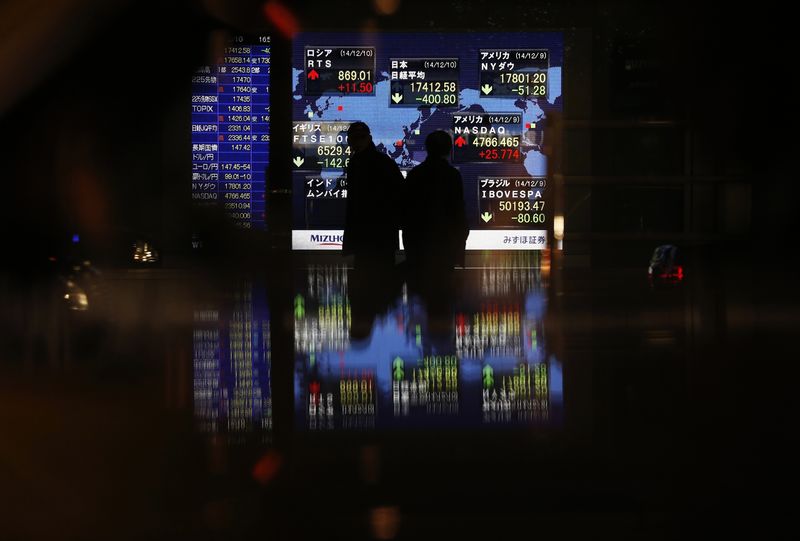 © Reuters. Passersby are silhouetted in front of an electronic board displaying Japan's Nikkei average and various countries' stock price index outside a brokerage in Tokyo