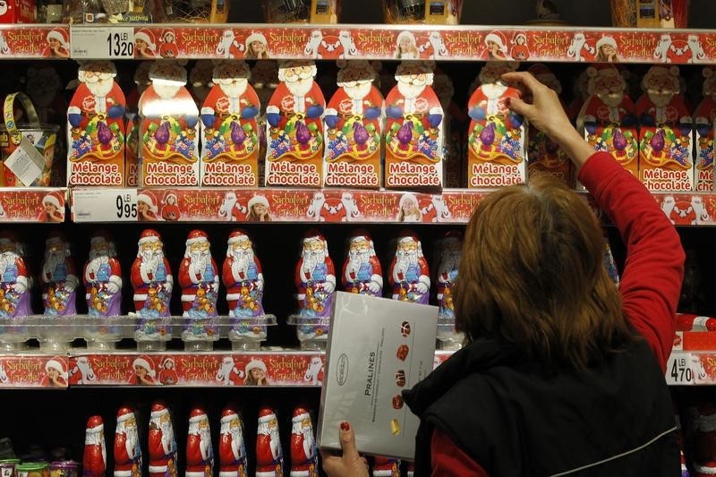 © Reuters. A worker arranges Santa Claus chocolate figurines on a shelf as shoppers take care of their last-minute Christmas gift needs in a mall in Bucharest