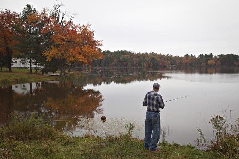 © Reuters. With the fall colors reflected in a lake, a man fishes for bass as it rains in Jeffersonville, New York