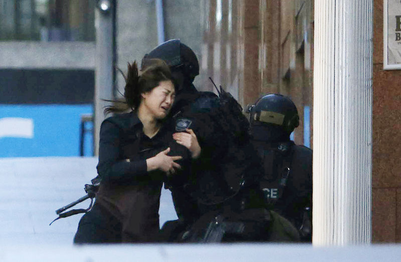 © Reuters. Mulher libertada corre em direção a um policial em frente a uma cafeteria onde pessoas são mantidas reféns, em Sydney 