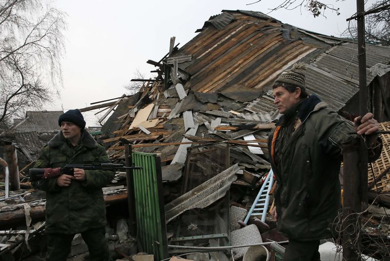 © Reuters. A Pro-Russian rebel and a local citizen stand in front of a house, which according to locals was destroyed by shelling last week, in the town of Gorlovka northeast of Donetsk