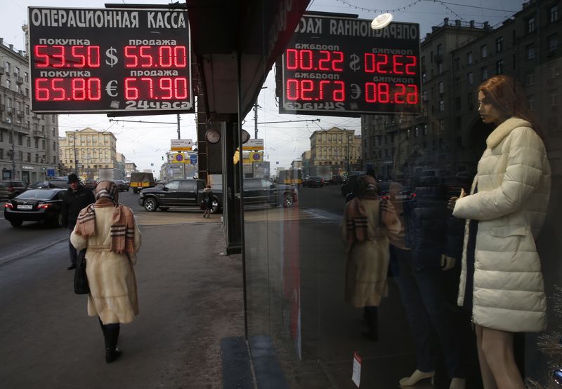 © Reuters. People walk along a street past a board showing currency exchange rates in Moscow