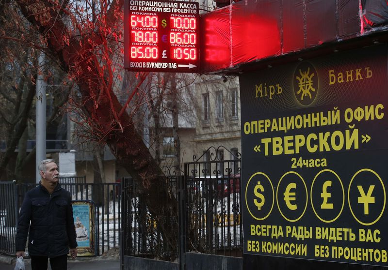 © Reuters. A man walks past a building and a board showing currency exchange rates in Moscow