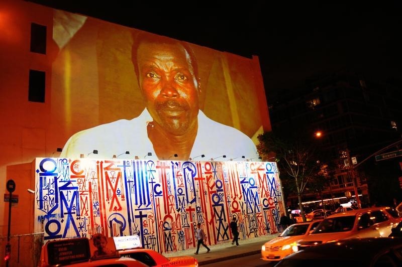 © Reuters. Passersby walk under a projection that is part of the non-profit organization Invisible Children's "Kony 2012" viral video campaign, in New York