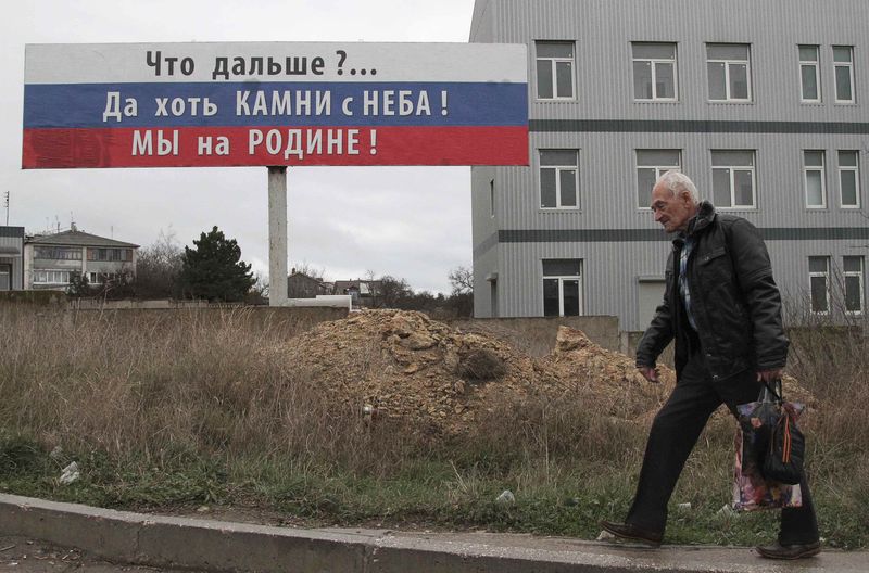 © Reuters. Homem caminha em frente a uma placa em russa na qual se lê "O que virá depois? Ao menos as pedras vêm do céu! Estamos em casa!", no porto de Sebastopol, na Crimeia anexada pela Rússia