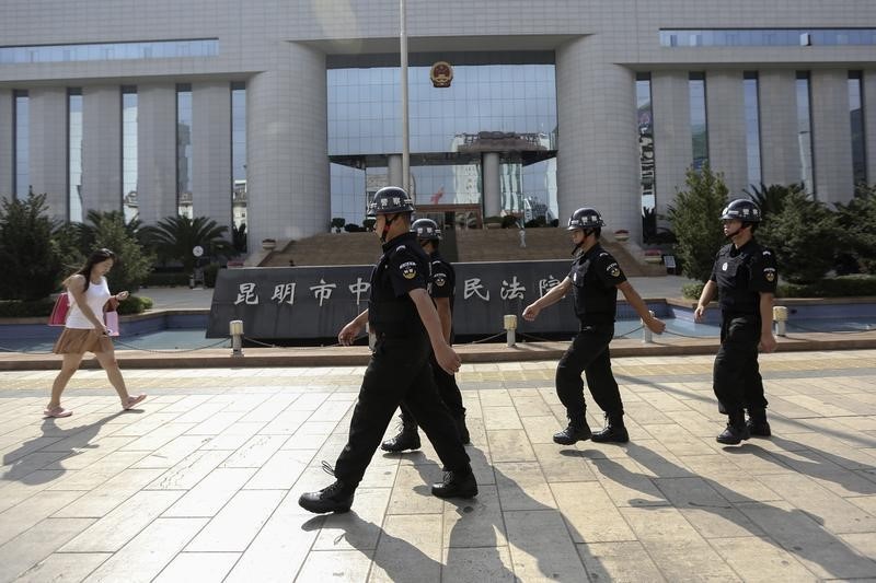 © Reuters. Policemen patrol as a woman walks past in front of a court, where a trial of suspects of the Kunming railway station attack is taking place, in Kunming
