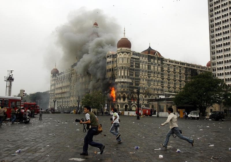 © Reuters. Photographers run past a burning Taj Mahal Hotel during a gun battle in Mumbai