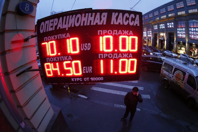 © Reuters. A man stands next to a building under a board showing currency exchange rates in Moscow