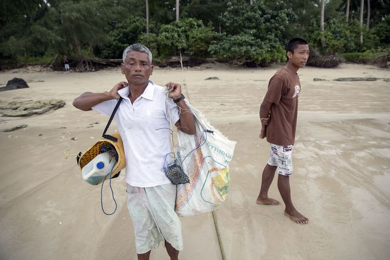 © Reuters. Hong Klathalay carries gear on his way to his fishing boat n Khao Lak