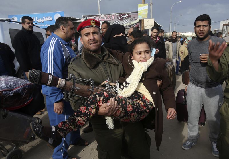© Reuters. A member of the Palestinian security forces carries a girl as she waits to cross into Egypt at the Rafah crossing between Egypt and the southern Gaza Strip