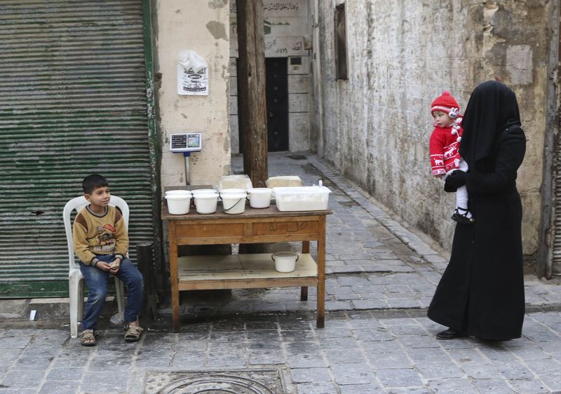 © Reuters. A woman carries a child as she walks past a boy selling yogurt along a street in Aleppo's Bab al-Hadeed district