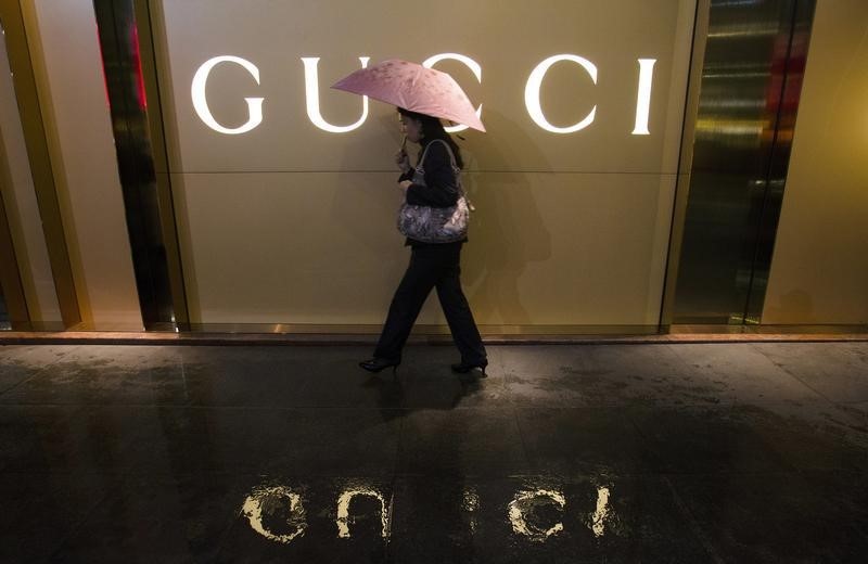 © Reuters. A woman holding an umbrella walks past a company logo of a Gucci boutigue outside a shopping mall amid rainfalls in central Guangzhou
