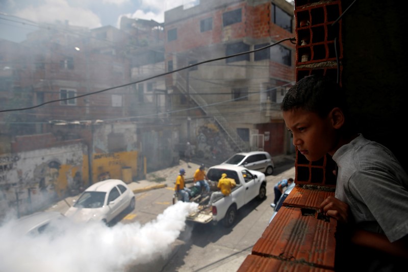 © Reuters. Menino observa trabalhadores aplicando remédio contra mosquito da dengue em rua de Caracas