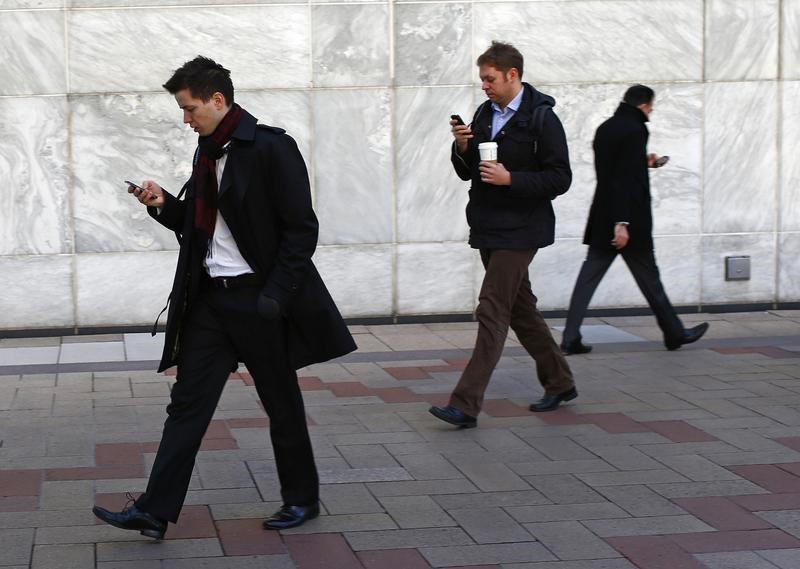 © Reuters. Workers look at their phones while walking at the Canary Wharf business district in London