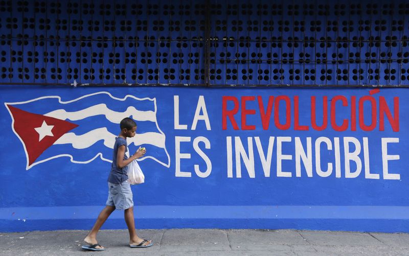 © Reuters. A boy walks past a graffiti reading "The revolution is invincible" in Havana