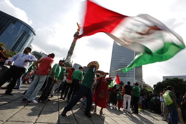 © Reuters. A Mexican soccer fan waves a Mexican national flag as he celebrates the 0-0 draw between Mexico and Brazil in their 2014 World Cup soccer match, at the Angel of Independence monument in Mexico City