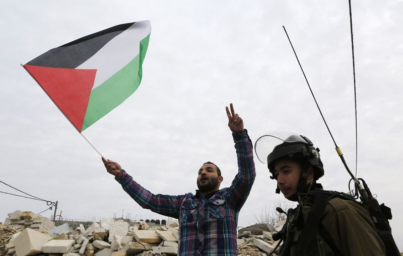 © Reuters. Manifestante palestino segura uma bandeira da Palestina perto de um soldado israelense