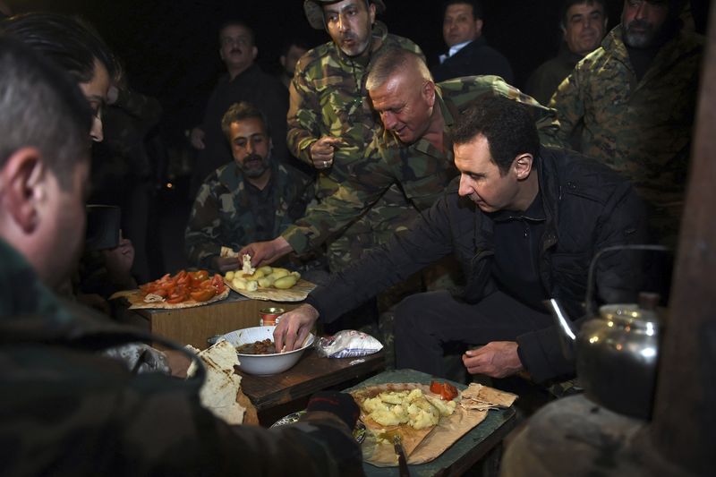© Reuters. Syrian President Bashar al-Assad (R) eats with soldiers during a visit to Jobar, northeast of Damascus