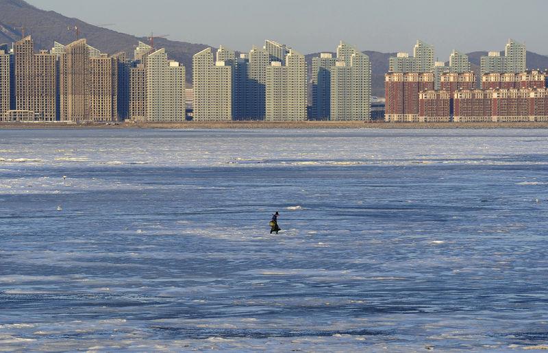 © Reuters. A fisherman walks on the partially frozen Jinzhou Bay of the Bohai Sea near residential construction sites, in Dalian