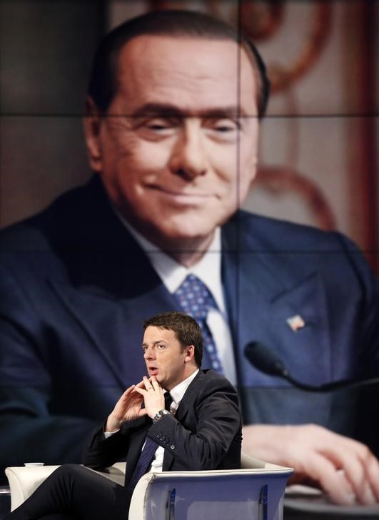 © Reuters. Italy's  Prime Minister Matteo Renzi gestures as a picture of former Prime Minister Silvio Berlusconi is seen on a large screen behind him during television talk show "Porta a Porta" (Door to Door)  in Rome