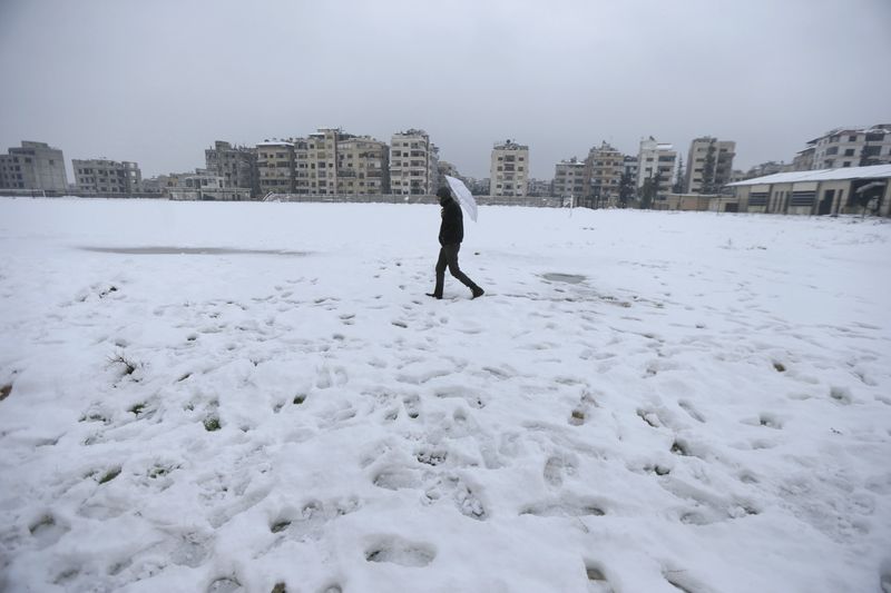 © Reuters. A man holds an umbrella as he makes his way through a road covered with snow in the Duma neighborhood of Damascus