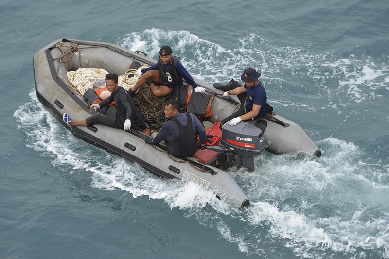 © Reuters. Indonesian navy divers sit in an inflatable boat after conducting operations to lift the tail of AirAsia QZ8501 in the Java sea