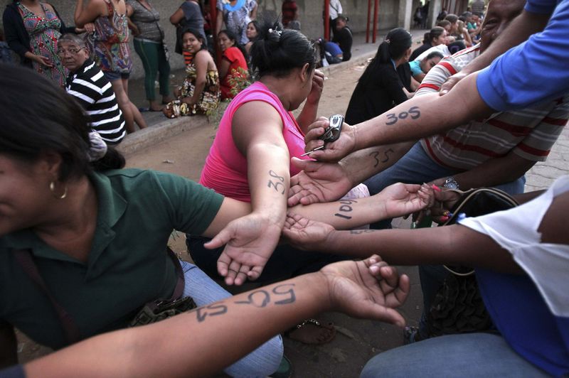 © Reuters. People show numbers written on their arms with the order they should enter at the state-run Bicentenario supermarket in Maracaibo