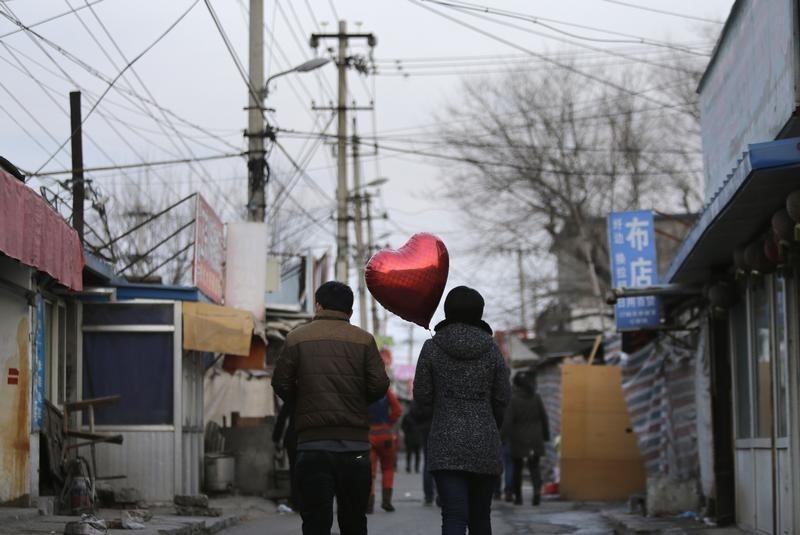 © Reuters. A woman holding a heart-shaped balloon walks with her partner at a residential area for migrant workers on Valentine's Day in Beijing