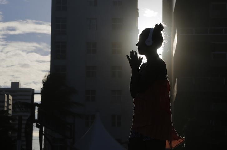 © Reuters. A woman listens to music as the sun sets as seen between buildings on Boa Viagem beach in Recife