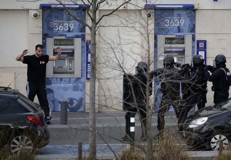 © Reuters. A suspect in a hostage taking situation is detained by members of special French RAID forces outside the post offices in Colombes outside Paris