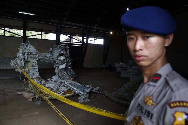 © Reuters. Police officer stands near part of the fuselage of crashed AirAsia Flight QZ8501 inside a storage facility at Kumai port in Pangkalan Bun