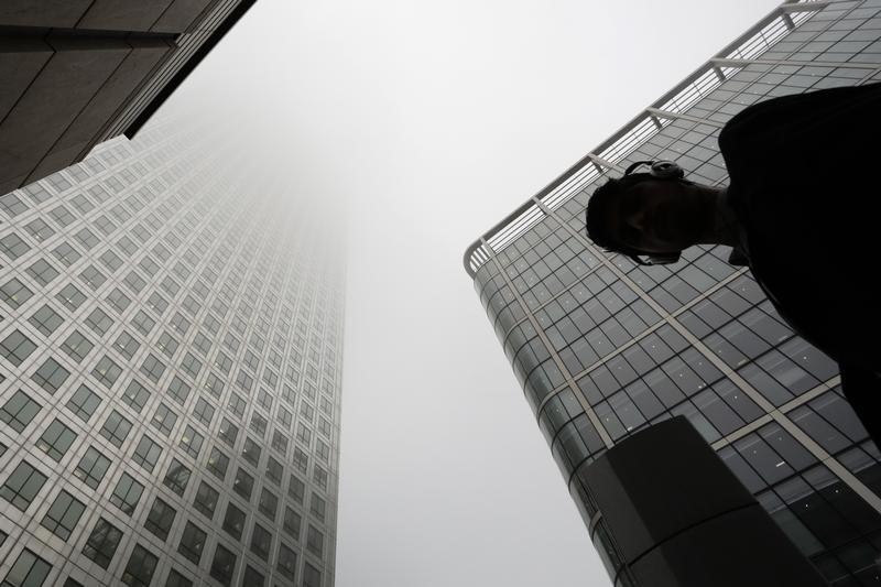 © Reuters. Man walks past a building in the morning mist at London's financial district of Canary Wharf