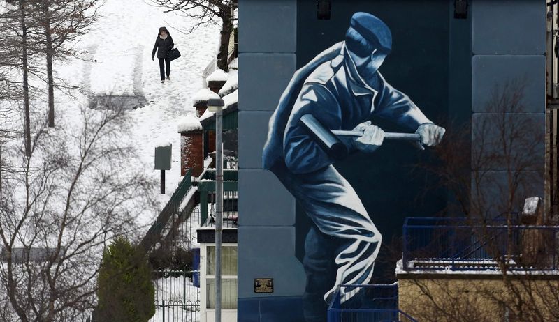 © Reuters. A woman walks towards a mural after heavy snowfall in Londonderry