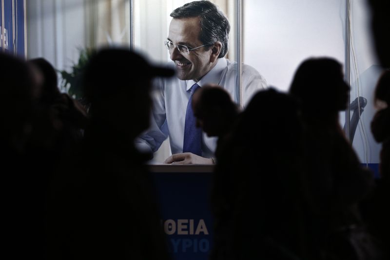 © Reuters. People are silhouetted as they walk past an image of Greece's PM and leader of ruling conservative New Democracy party Samaras displayed at the party's election kiosk in Athens