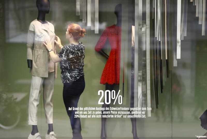 © Reuters. A slogan offers 20 percent of price reduction as an employee dresses a dummy in a display window of a cloth shop in Zurich