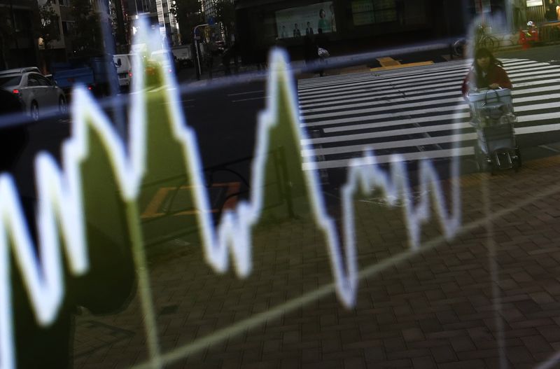 © Reuters. A woman pushing  cart is reflected on electronic board showing graph of recent fluctuations of Japan's Nikkei average outside a brokerage in Tokyo