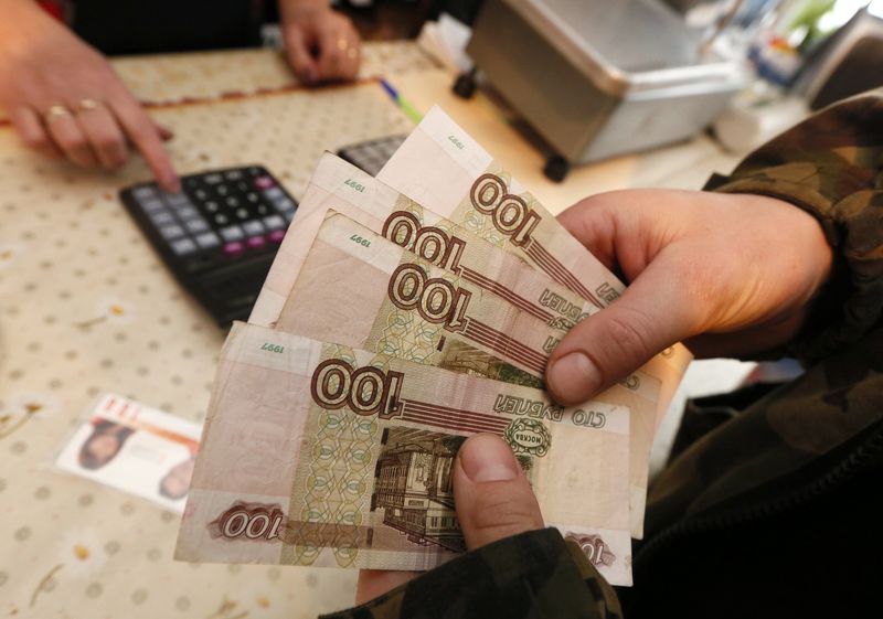 © Reuters. A customer holds 100-rouble banknotes while visiting a local grocery store in the village of Verkhnyaya Biryusa outside the Russian Siberian city of Krasnoyarsk