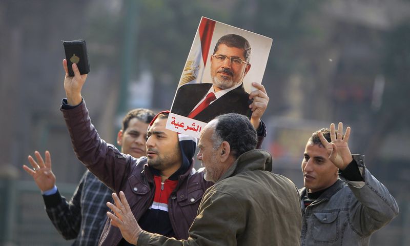 © Reuters. Supporters of the Muslim Brotherhood and ousted Egyptian President Mohamed Mursi hold a copy of the Koran and Mursi's picture at Talaat Harb Square, in Cairo