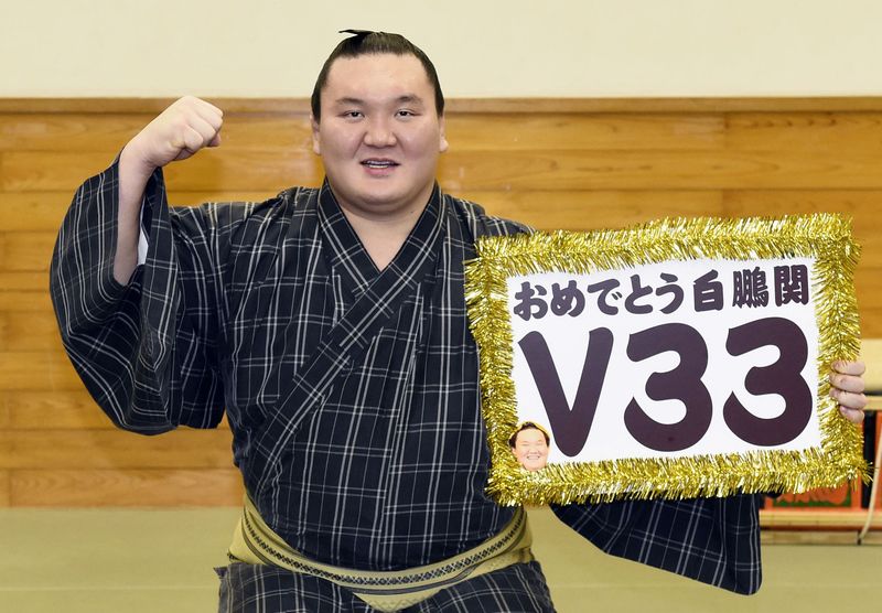 © Reuters. Mongolian-born grand sumo champion Yokozuna Hakuho poses for photos with a board reading "Congrats Hakuho V33" after winning the New Year Grand Sumo Tournament in Tokyo