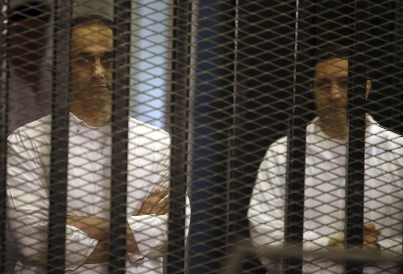 © Reuters. Gamal and Alaa Mubarak, sons of Hosni Mubarak, stand behind bars during their trial at the police academy, on the outskirts of Cairo