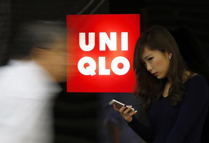 © Reuters. A woman holding her mobile phone stands next to a logo of Fast Retailing's Uniqlo outside its store in Tokyo