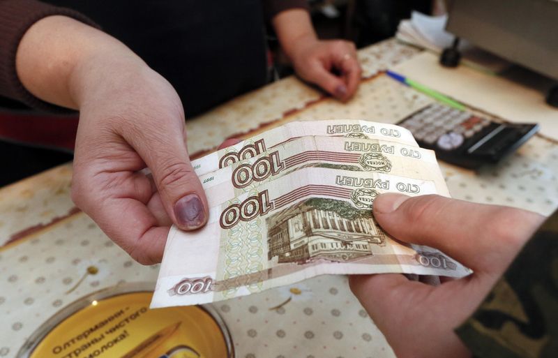 © Reuters. A customer hands over 100-rouble banknotes to the saleswoman of a local grocery in the village Verkhnyaya Biryusa