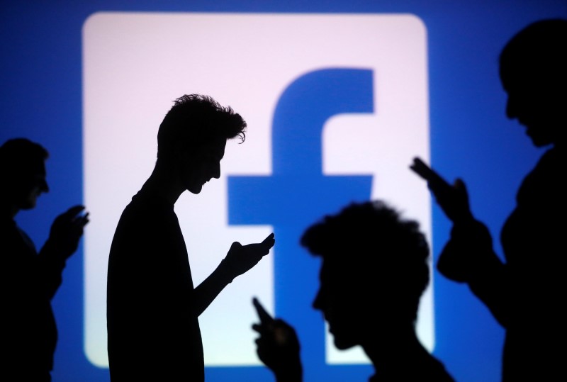 © Reuters. Pessoas posam usando celulares em frente ao logo do Facebook para foto de ilustração