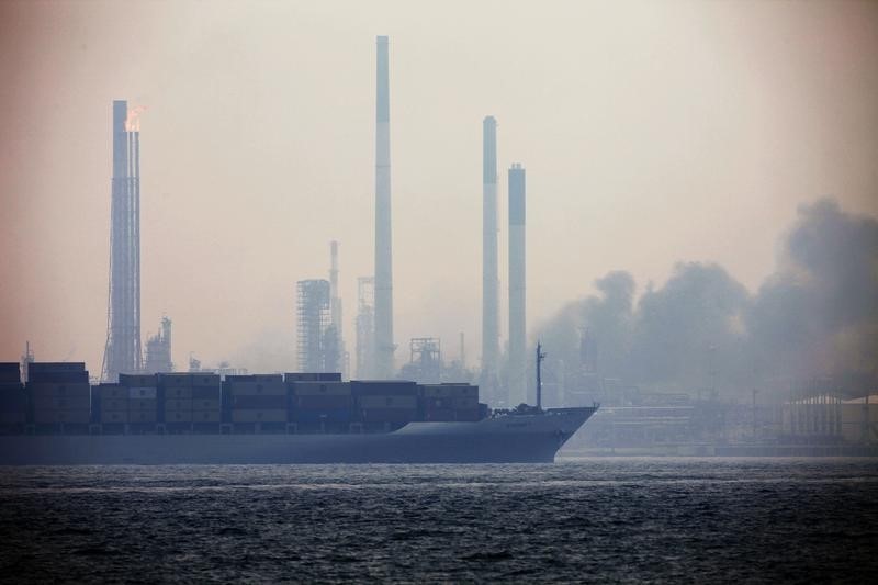 © Reuters. A container vessel sails past as smoke billows from Royal Dutch Shell's Pulau Bukom offshore petroleum complex in Singapore