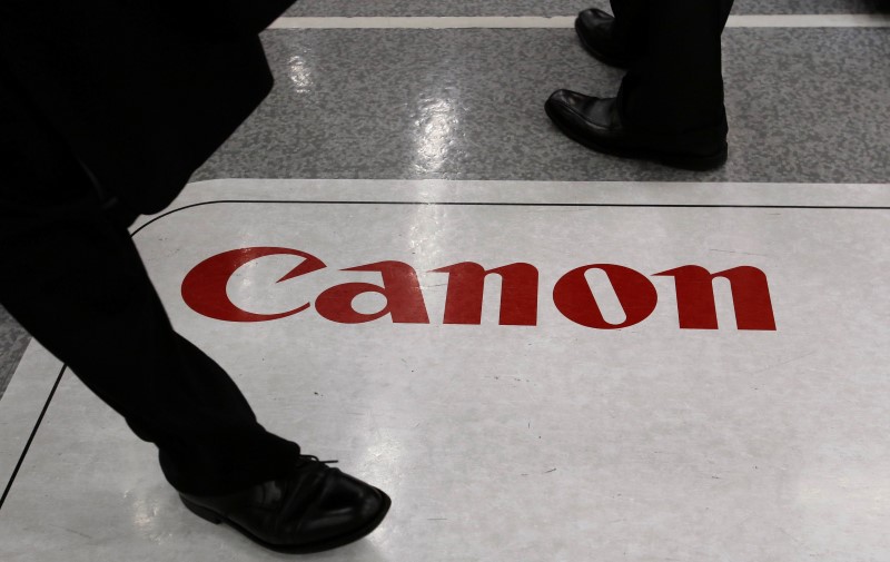 © Reuters. Men walk on an advertisement for Canon Inc at an electronics retail store in Tokyo