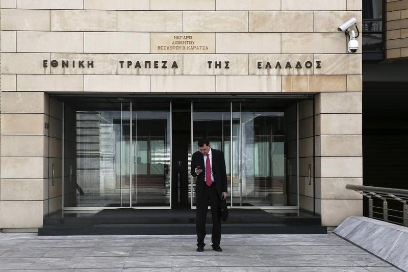 © Reuters. A man checks his mobile phone as he stands at the entrance of the National Bank headquarters in Athens